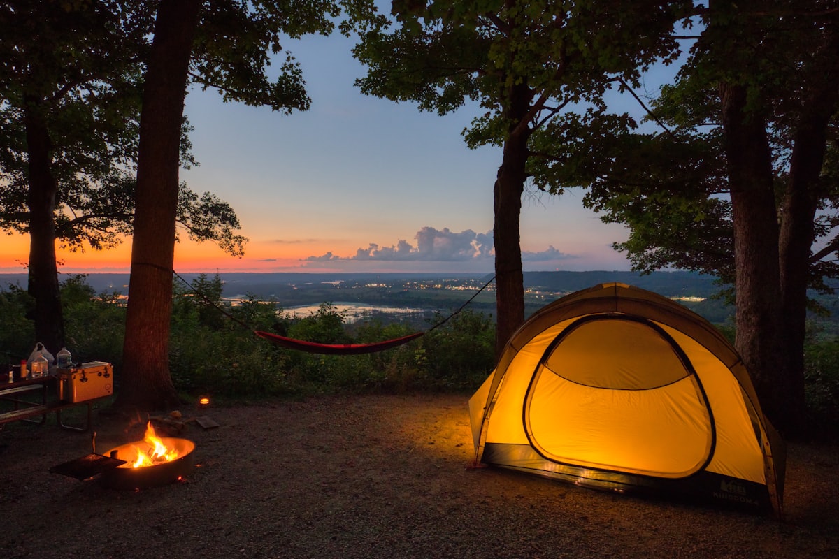 A tent in the woods at sunset with a campfire glow - solo camping for two campfire cooking
