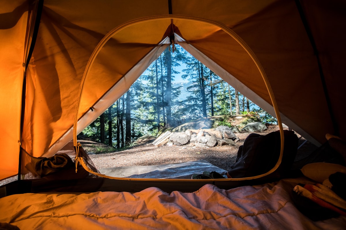 An orange tent pitched among green trees at a wooded campsite - solo camping for two gear repair