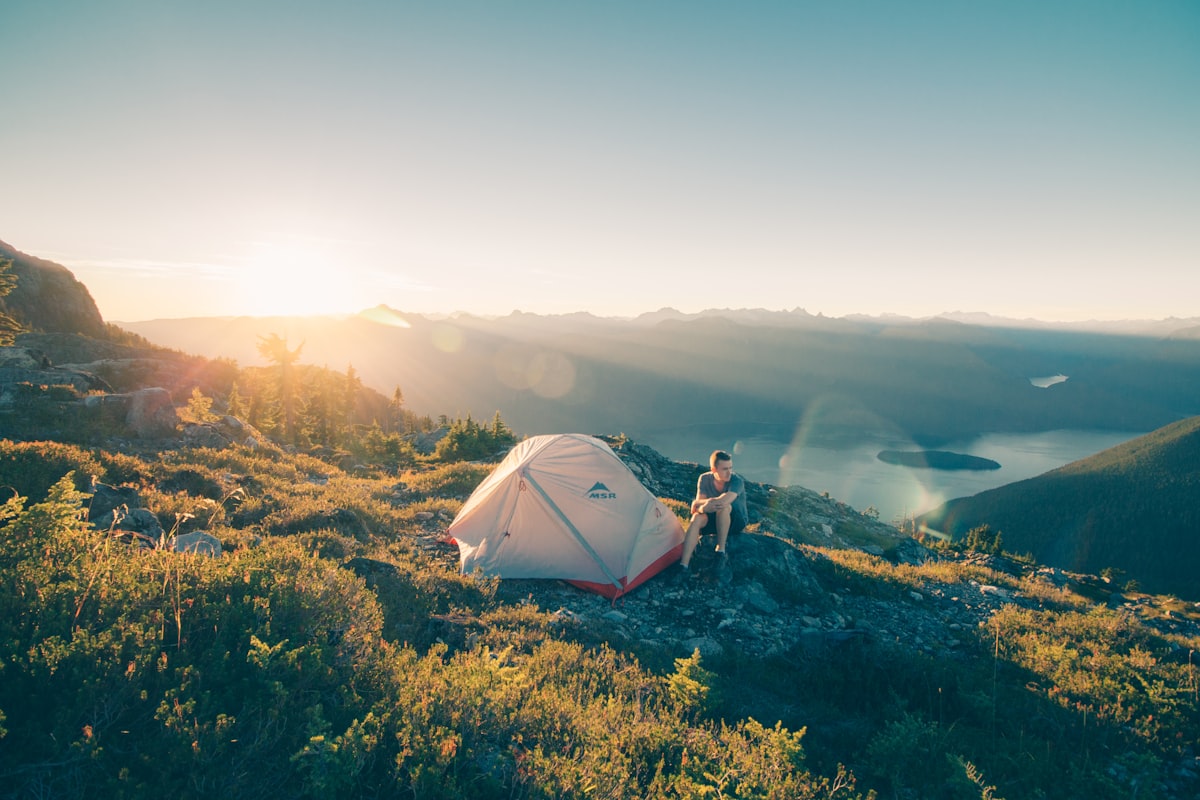 A person sitting alone on a rock beside a tent in the wilderness - solo camping mental health benefits